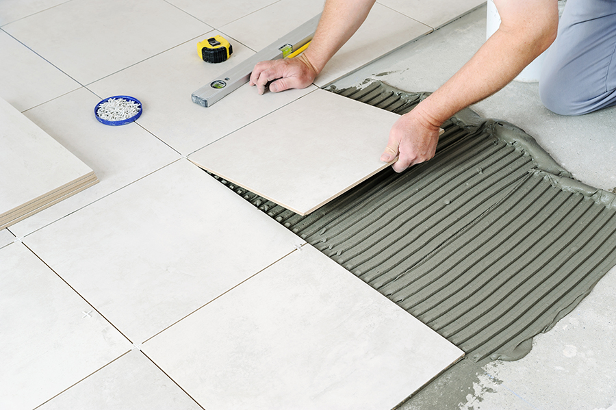 The hands of the worker are laying  the ceramic tile on the floor.